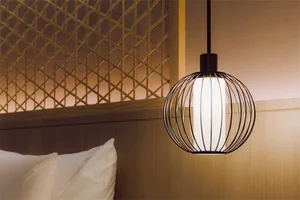 A minimalist bedroom with textured wood walls, white bedding, and a modern pendant light.