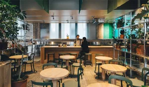 Industrial-style restaurant interior with wooden tables, concrete flooring, and metal bar counter.