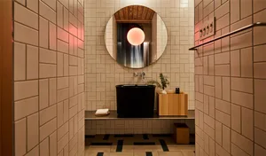 Bathroom interior featuring minimalist design with concrete tiles and black bathtub with a circular mirror above it.