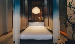 A minimalist bedroom with an enclosed bed featuring white textured canvas bedding and a hanging pendant light.