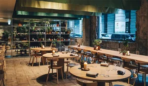 Interior of a modern food court with wooden tables and chairs, greenery, and a wine rack.