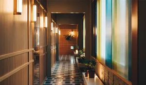 A modern interior corridor with wooden walls and white flooring, illuminated by warm light fixtures.