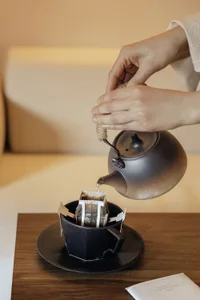 Person preparing coffee in a black ceramic cup over a coffee filter bag