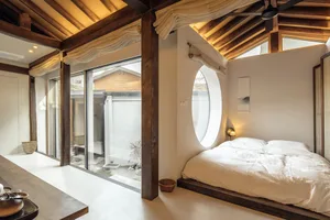 A modern minimalist bedroom with a white bed, wooden frame, and circular window.