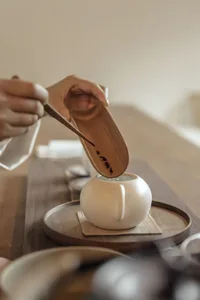 A minimalist tea ceremony setup featuring a white ceramic teapot and a wooden spoon on a wooden tray.