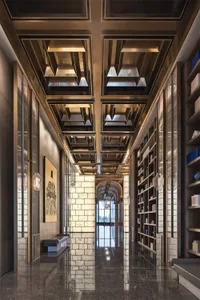 A modern corridor with marble walls, a ceiling with geometric lighting fixtures, and bookshelves filled with books.
