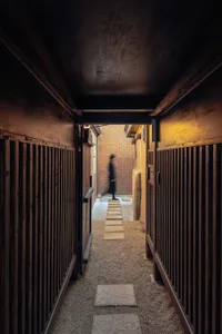 A minimalist corridor with wooden walls and a sandy floor featuring a person walking.