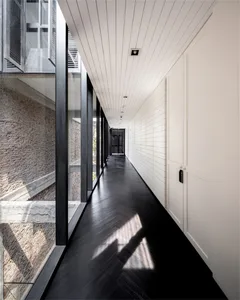 A modern white corridor with large glass windows and dark wooden flooring.