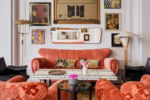 A modern living room features furniture with vibrant orange upholstery, complemented by colorful abstract art and a terrazzo 