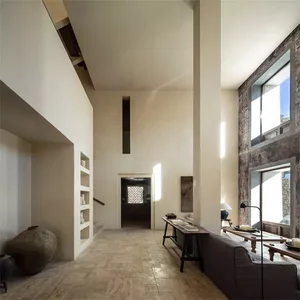 Modern minimalist living room with concrete flooring and walls, featuring a dark couch and a low table with books and decorat