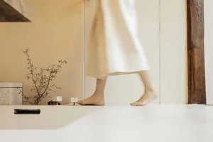A minimalist room with white walls and a white floor, featuring a white plant and a wooden beam