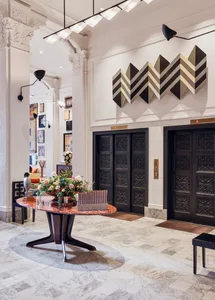 A luxurious lobby with marble floors, ornate black doors, and a floral centerpiece on a red marble table.