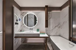 Modern bathroom with marble tiles, round illuminated mirror, and freestanding bathtub.