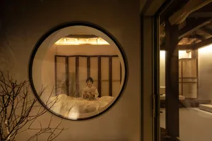 A woman reading a book in a modern bedroom with a circular window and wooden screens.