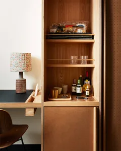 Modern home bar shelving unit made of wood, with various items on the shelves, including bottles, glasses, and packaging.