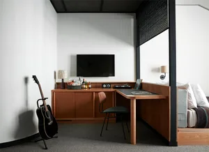 A modern studio apartment featuring a minimalist workspace, a guitar leaning against the wall, and a cozy sleeping area with 
