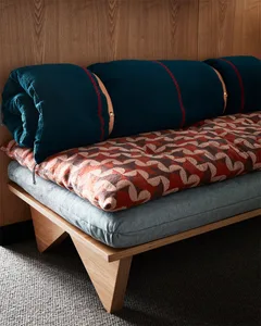 A cushion and blanket with an industrial aesthetic, featuring textured fabrics and geometric patterns, placed on a wooden pla