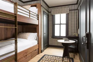 A modern bedroom featuring wooden bunk beds with metal railings and plaid bedding on the upper bunk, a striped rug, a small r