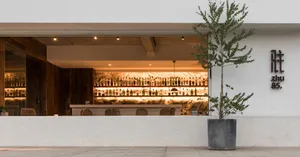 A modern restaurant bar with a concrete façade and illuminated shelves showcasing numerous bottles.