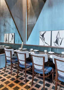 Modern restaurant interior with wooden flooring, metallic chairs, and plaster walls