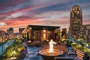 A rooftop patio with seating areas, a fire pit, and cityscape view during sunset.
