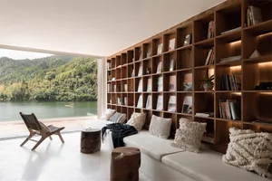A minimalist living space featuring a large bookshelf filled with books and a cozy seating area by a waterfront.