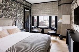 A modern hotel bedroom with patterned walls, a large bed, and a view of the city through a window.
