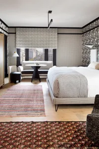 A modern bedroom featuring wood flooring, patterned wallpaper, and a striped bedspread.