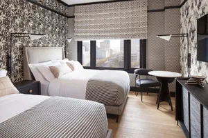 A modern hotel room featuring a bed with striped bedding and a window overlooking a cityscape, complemented by textured wallp