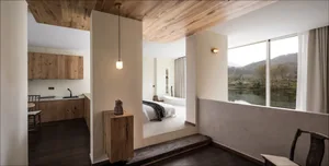 Modern minimalist bedroom featuring a bed with a wooden headboard and a wooden floor, with a view of the mountains through th