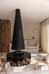 A minimalist living room featuring a modern fireplace with metallic cone-shaped chimney, surrounded by white furniture and a