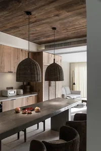 A modern minimalist kitchen with a concrete countertop, featuring a long rectangular table with a bowl of pomegranates and tw
