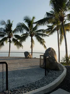 Concrete path with large rocks and palm trees overlooking the ocean.