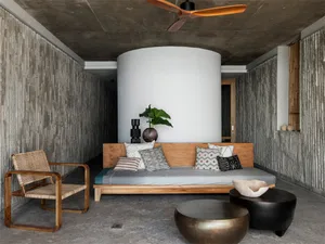 A minimalist living room with concrete walls and a wooden sofa adorned with patterned cushions.
