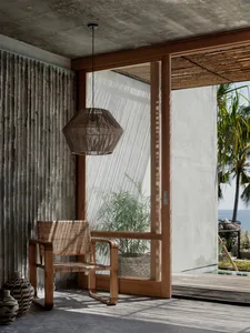 A minimalist patio with concrete walls, wood furniture, and natural fiber lampshade, featuring a view of the sea.