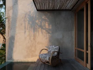A wooden chair with floral cushions on a patio with a concrete wall and a wooden door.