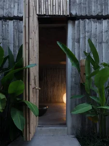 An open bamboo doorway constructed with concrete, illuminated by a nearby light.