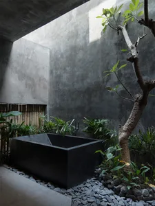 An industrial-style bathroom featuring a black stone bathtub surrounded by rocks and greenery.