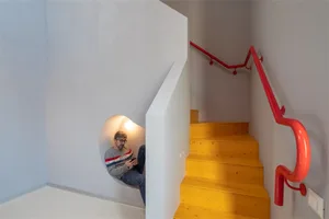 A modern industrial staircase with bright yellow wooden steps and a sleek red handrail.