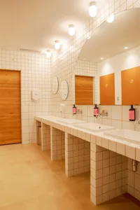 A modern industrial bathroom with white tiled walls and square tiles on the floor.