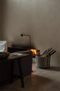 A minimalist living room with a wood floor, stone fireplace, and wicker basket filled with firewood.