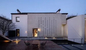 A minimalist residential exterior featuring a concrete structure with a grid of circular cutouts.