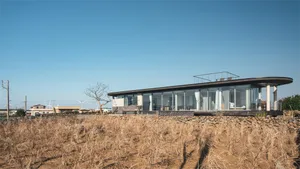 Modern house with glass exterior on a field of dry grass under a clear blue sky.