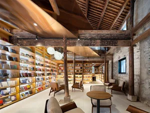 An industrial-style library interior with wooden beams, concrete floors, and glass walls.