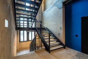 Industrial-style metal staircase indoors with concrete flooring and a blue door.