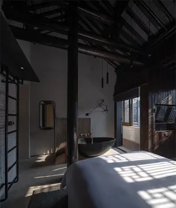 Interior of a minimalist bedroom with concrete walls and ceiling beams, featuring a black bathtub and a bed.