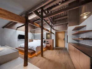 Modern minimalist bedroom with wooden floors, beams, and furniture, featuring a white bed and floating nightstands.