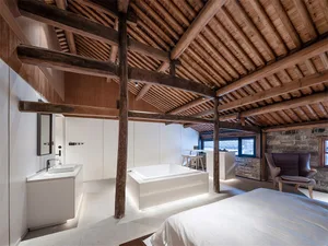 A modern bedroom with a concrete bathtub, minimalistic design, and exposed wooden beams on the ceiling.