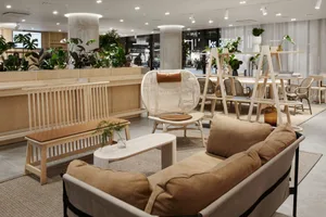 A modern lobby featuring wooden furniture, concrete walls, and various indoor plants, creating a welcoming atmosphere.