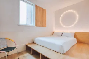 A modern, minimalist bedroom with a white bed and wooden furnishings